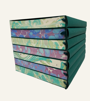 Tall stack of marbleized refillable journal inserts in blue and burgundy and green and ivory with attached green satin bookmark