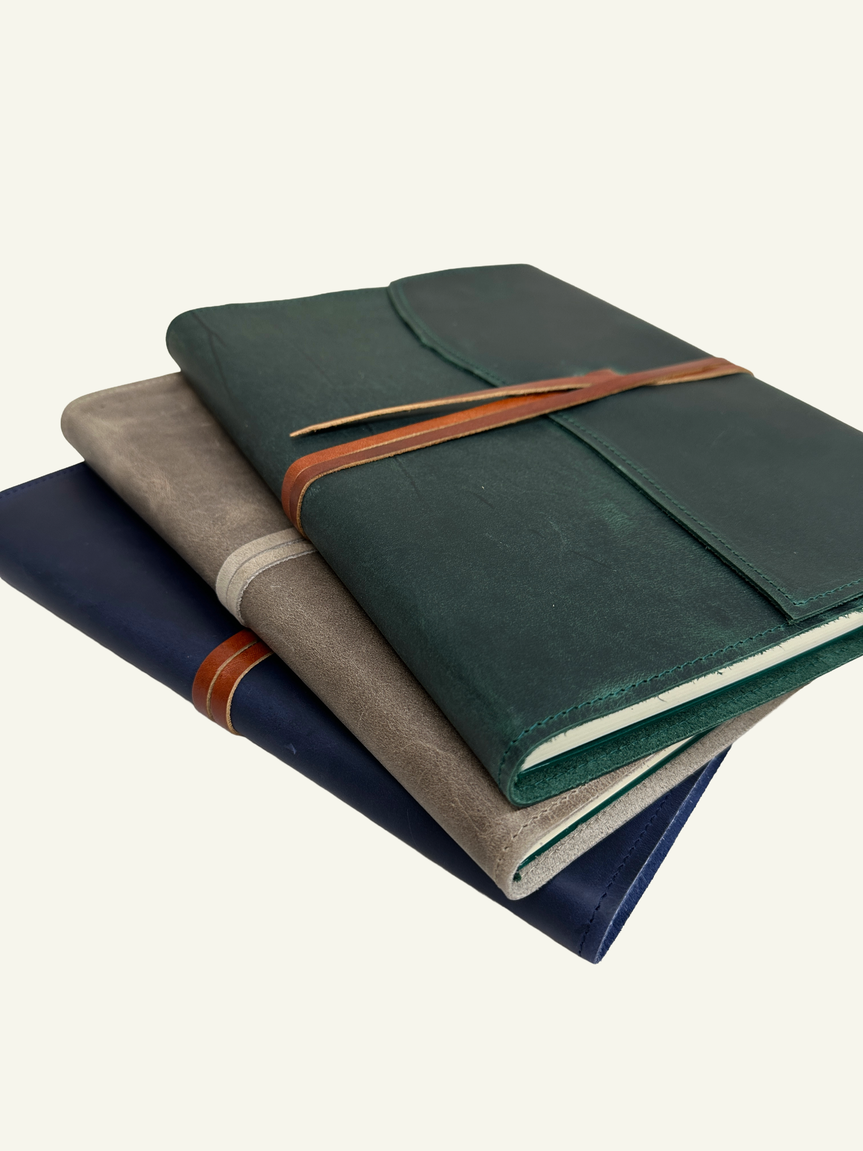 Forest green, stone taupe, and midnight blue refillable leather journals stacked together