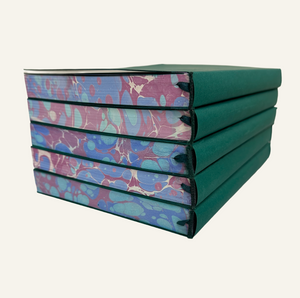 Stacked refillable journal inserts with marbleized edges in blue and burgundy and attached green bookmark