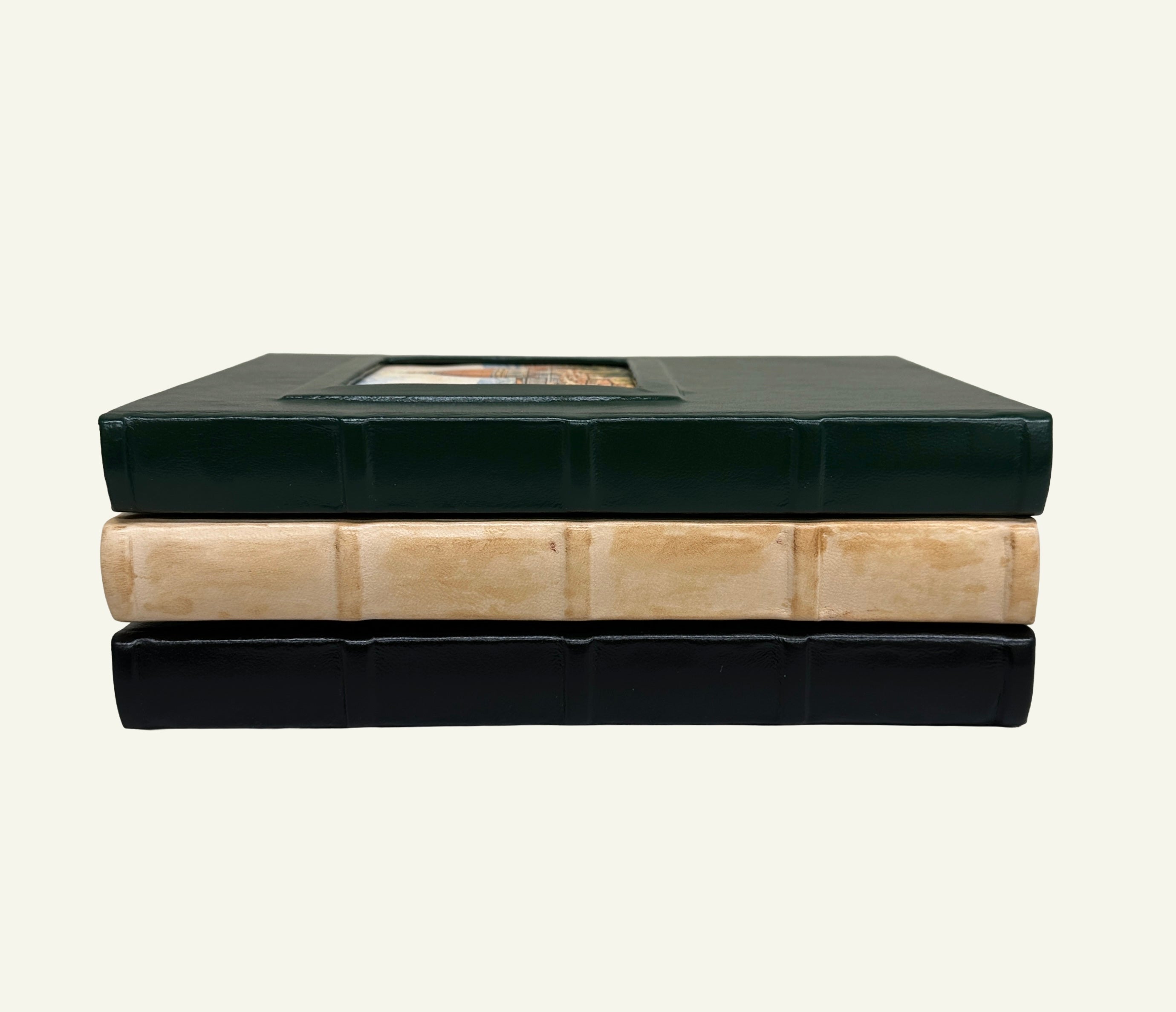 Stacked leather journals showing the square spine detailing and raised portrait window covers.