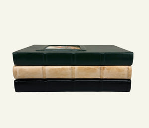 Stacked leather journals showing the square spine detailing and raised portrait window covers.