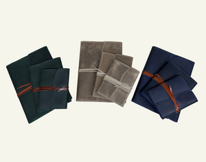 Three leather journals in dark green, taupe, and navy blue, shown in different sizes and tied with leather cords.