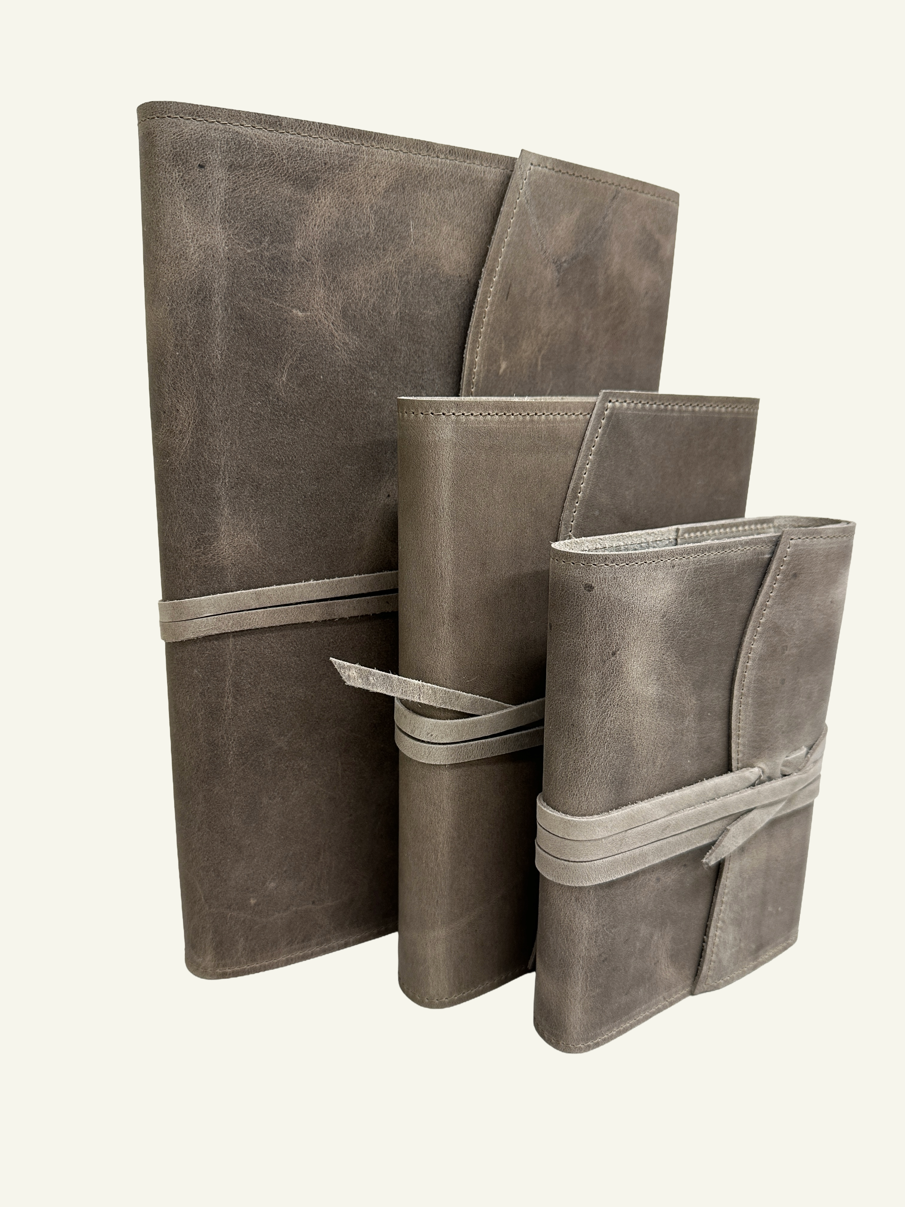 Three stone taupe leather journals in different sizes standing upright, showcasing their handcrafted leather covers and wraparound cords.