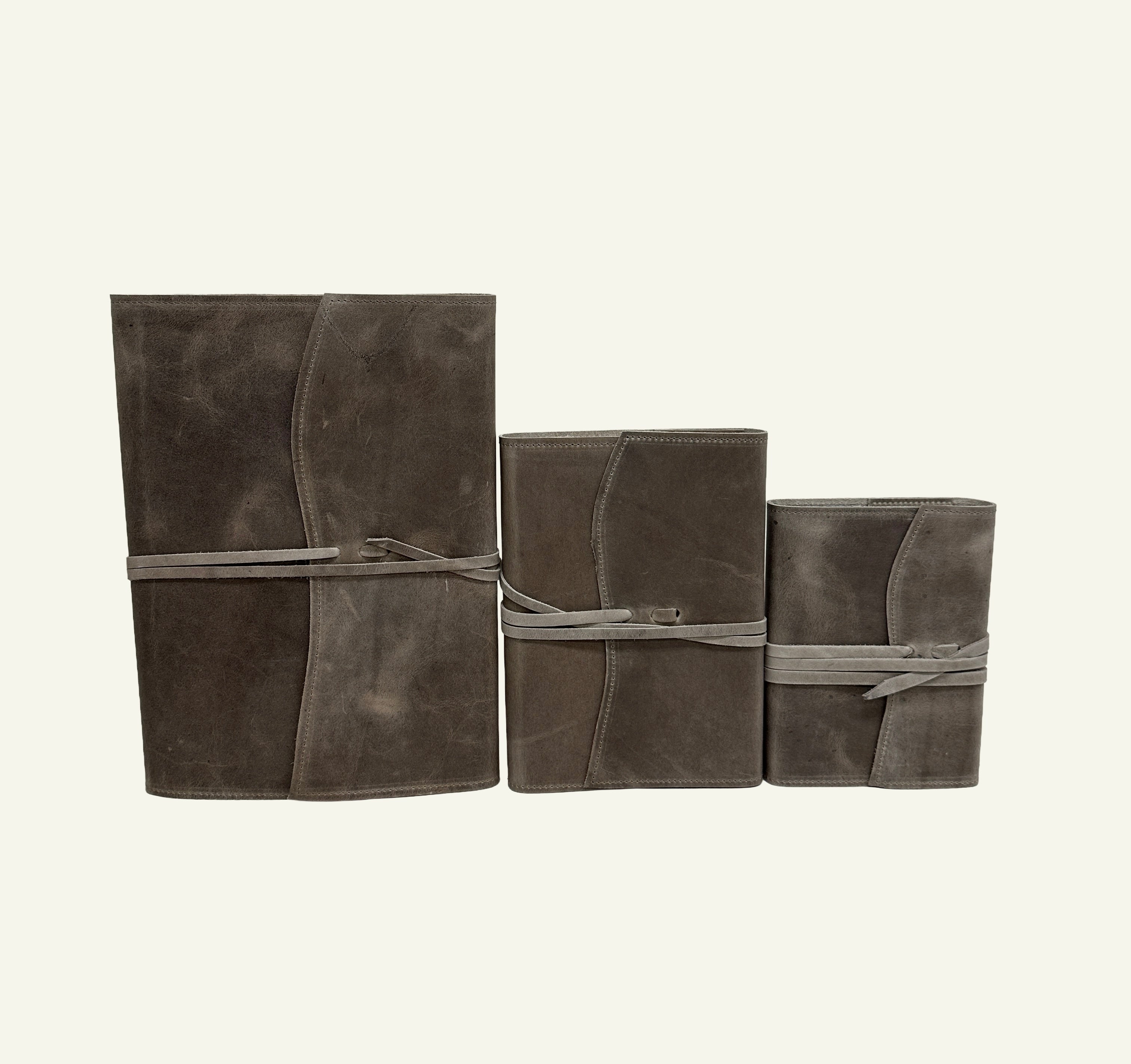 Three stone taupe leather journals in small, medium, and large sizes, each wrapped with a matching leather cord.